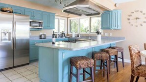 Una cucina con mobili color petrolio, un frigorifero in acciaio inossidabile, un forno a microonde e una grande isola con sgabelli da bar.