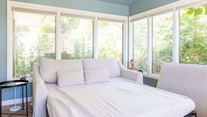 Camera da letto con un letto grande, una poltrona bianca e un tavolino. Diverse finestre offrono vista sul verde circostante.