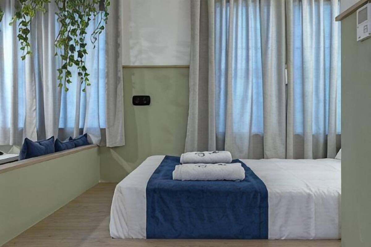A bedroom with a bed, window with curtains, and a bedside table.