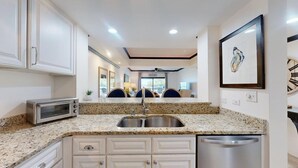 Una cocina con encimeras de granito, electrodomésticos de acero inoxidable, armarios blancos y lavavajillas integrado.