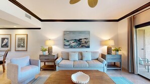 Una sala de estar con un sofá, dos mesitas de noche con lámparas, una mesa de centro con un cuenco decorativo y un cuadro en la pared.