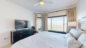 Habitación de hotel con cama, televisión, escritorio, silla, ventilador de techo y ventana con cortinas.