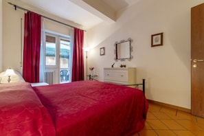 Une chambre à coucher avec un lit, une commode, un miroir et une fenêtre ornée de rideaux rouges.