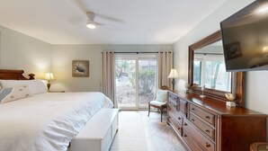 Une chambre à coucher comprenant un lit, une commode, une chaise, un téléviseur et une vue sur l’extérieur grâce à une porte coulissante.