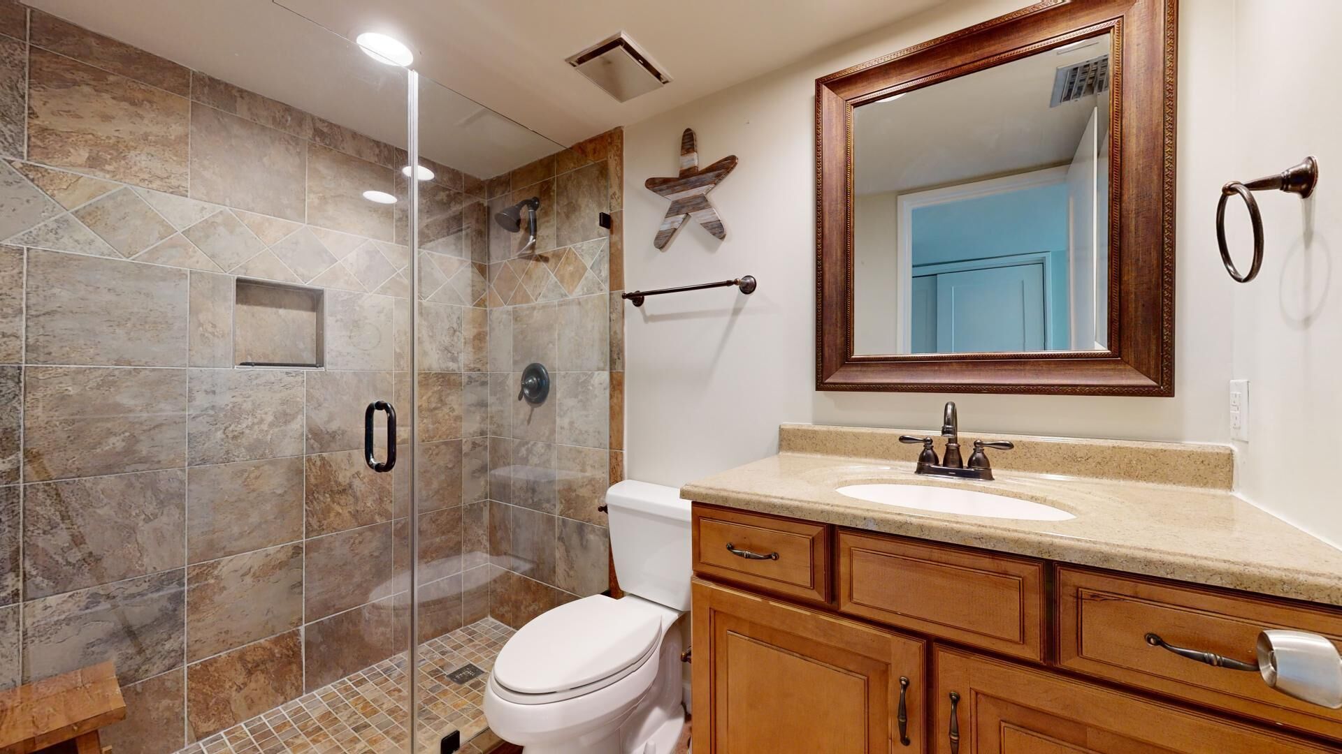 A bathroom with a glass-enclosed shower, a white toilet, wooden cabinets, a sink with a mirror, and a towel rack.