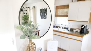 A modern kitchen with white cabinets, a wooden countertop, and a round mirror above a wicker vase with green foliage. - OBX Beach's, Natural Light, Roof Deck, Huge Home! (Kitty Hawk)