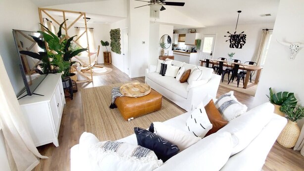 A spacious living room with a white sofa, a brown ottoman, and a dining area in the background. - OBX Beach's, Natural Light, Roof Deck, Huge Home! (Kitty Hawk)