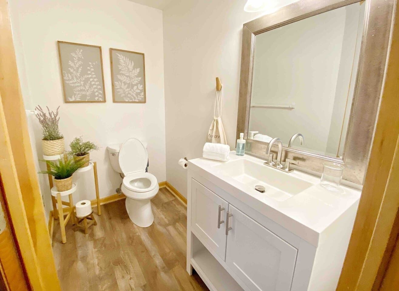 A bathroom with a toilet, sink, mirror, and two framed wall decorations.