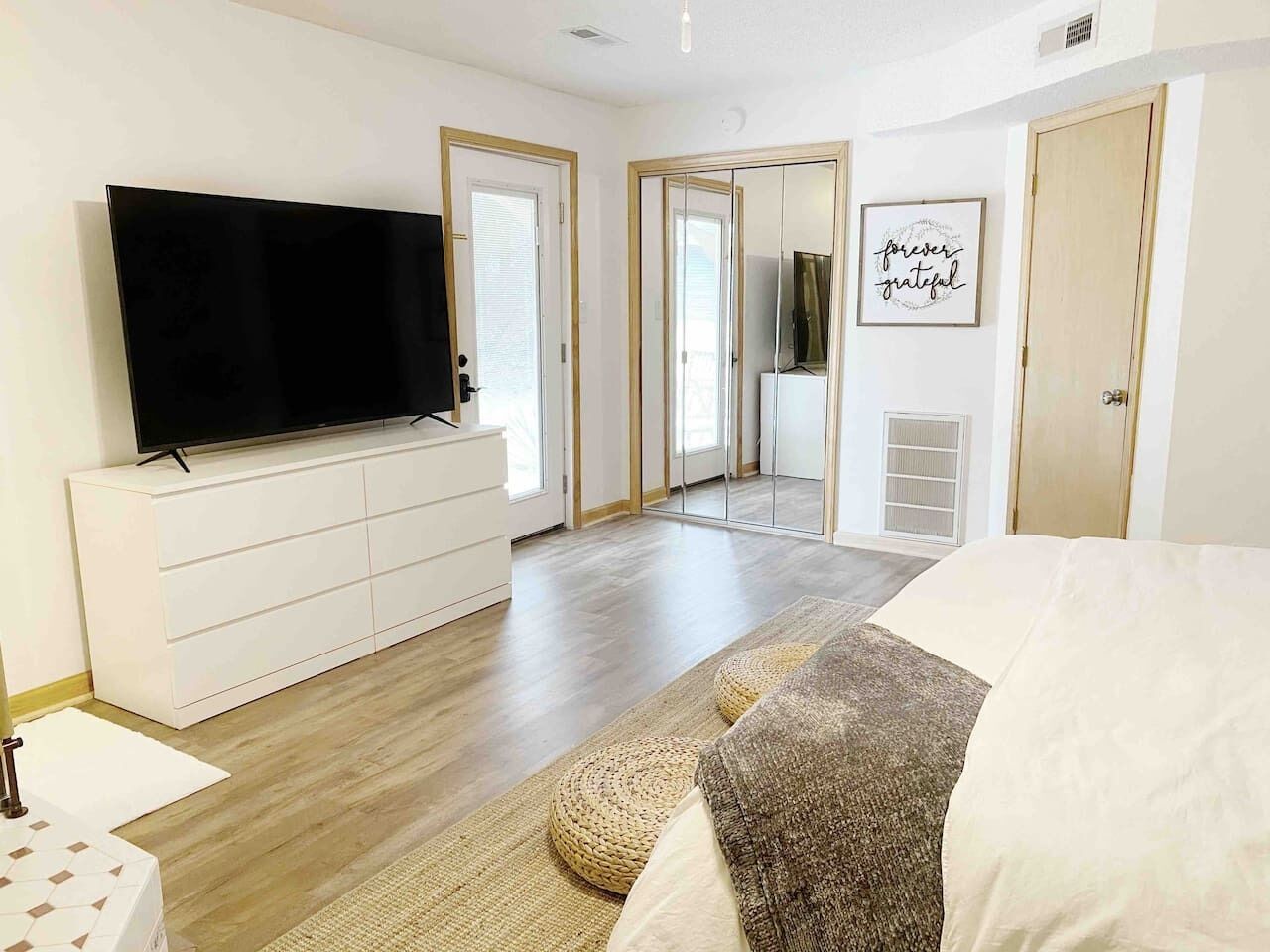 A modern bedroom with a flat-screen TV, a large mirror, and a motivational quote on the wall.
