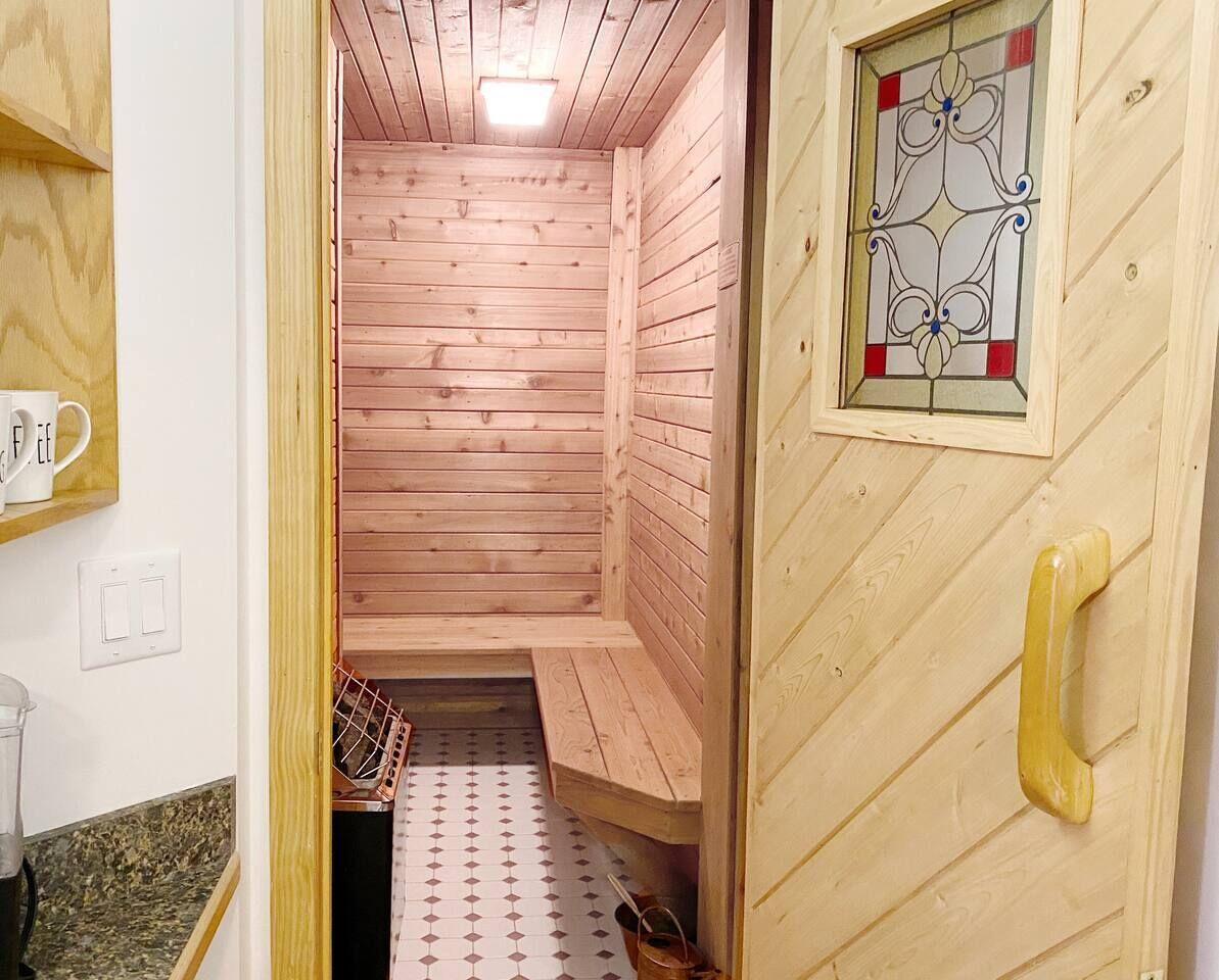 A wooden sauna with a bench, a door with a glass window, and a tiled floor.