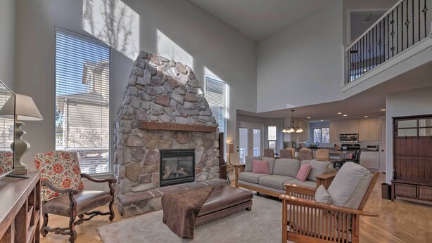 A spacious living room with a stone fireplace, a high ceiling, and a view of the kitchen. - Mountain-View Home < 15 Mi to Alta + Snowbird (Sandy)