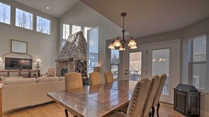 A spacious living room with a large wooden dining table, comfortable seating, a stone fireplace, and large windows offering views of the city. - Mountain-View Home < 15 Mi to Alta + Snowbird (Sandy)