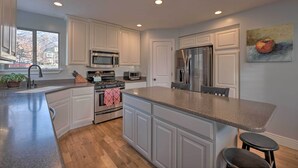 A modern kitchen with white cabinetry, stainless steel appliances, a granite countertop, and a large window providing a view of the outside. - Mountain-View Home < 15 Mi to Alta + Snowbird (Sandy)