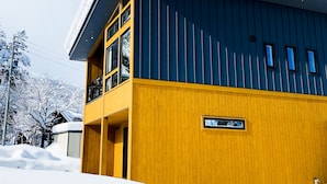 A two-story building with a yellow facade and a dark blue roof, surrounded by snow.