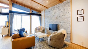 A modern living room with a stone wall, a flat-screen TV, and a large window with curtains.