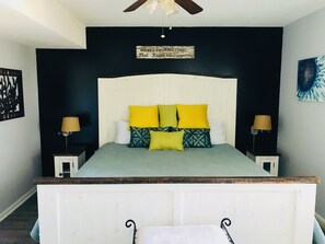 A bedroom with a bed, two bedside tables, a ceiling fan, and a wall-mounted sign.