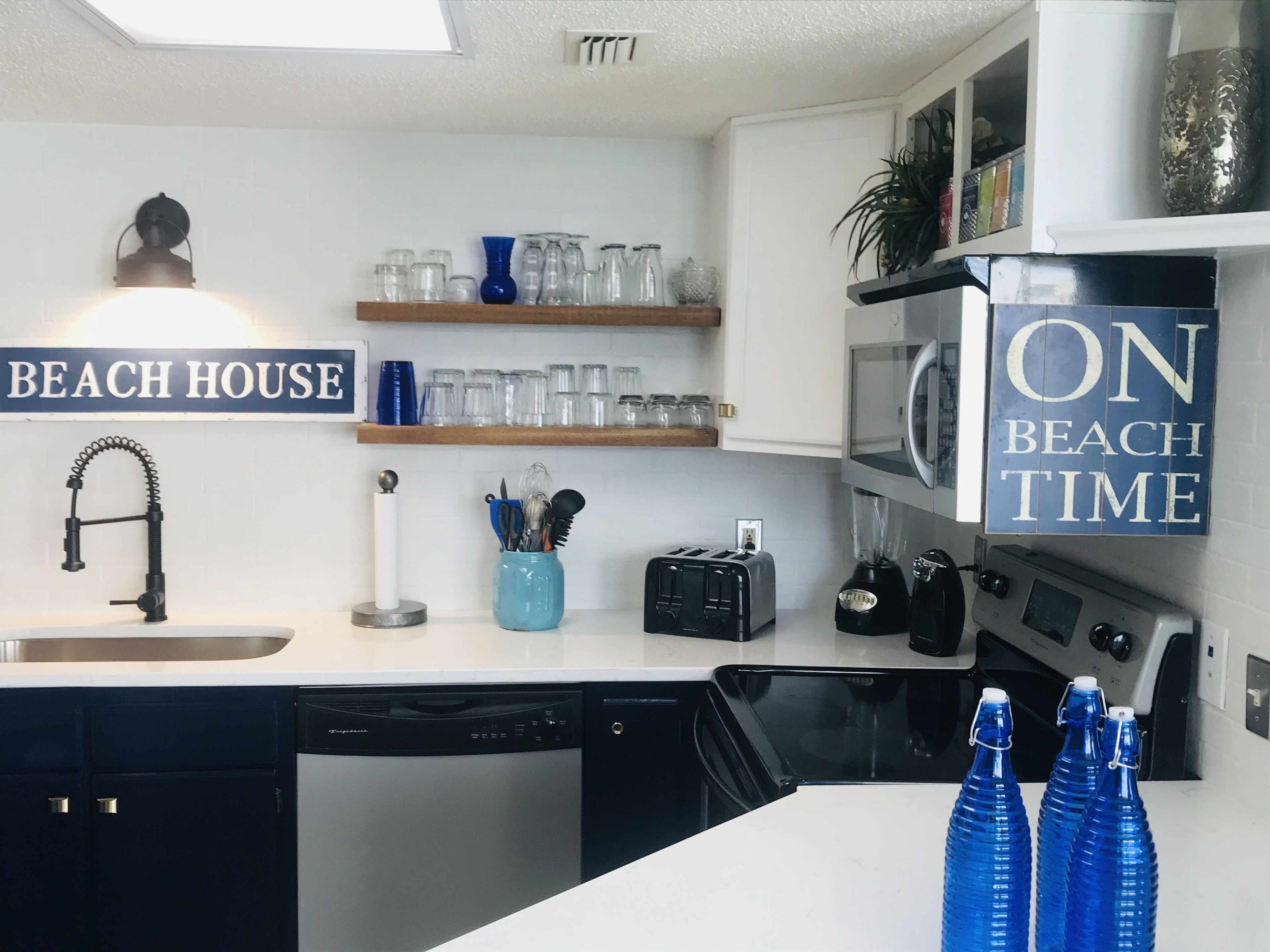 Una cocina moderna con pileta, lavavajillas, tostadora, licuadora y un cartel que dice "BEACH HOUSE".