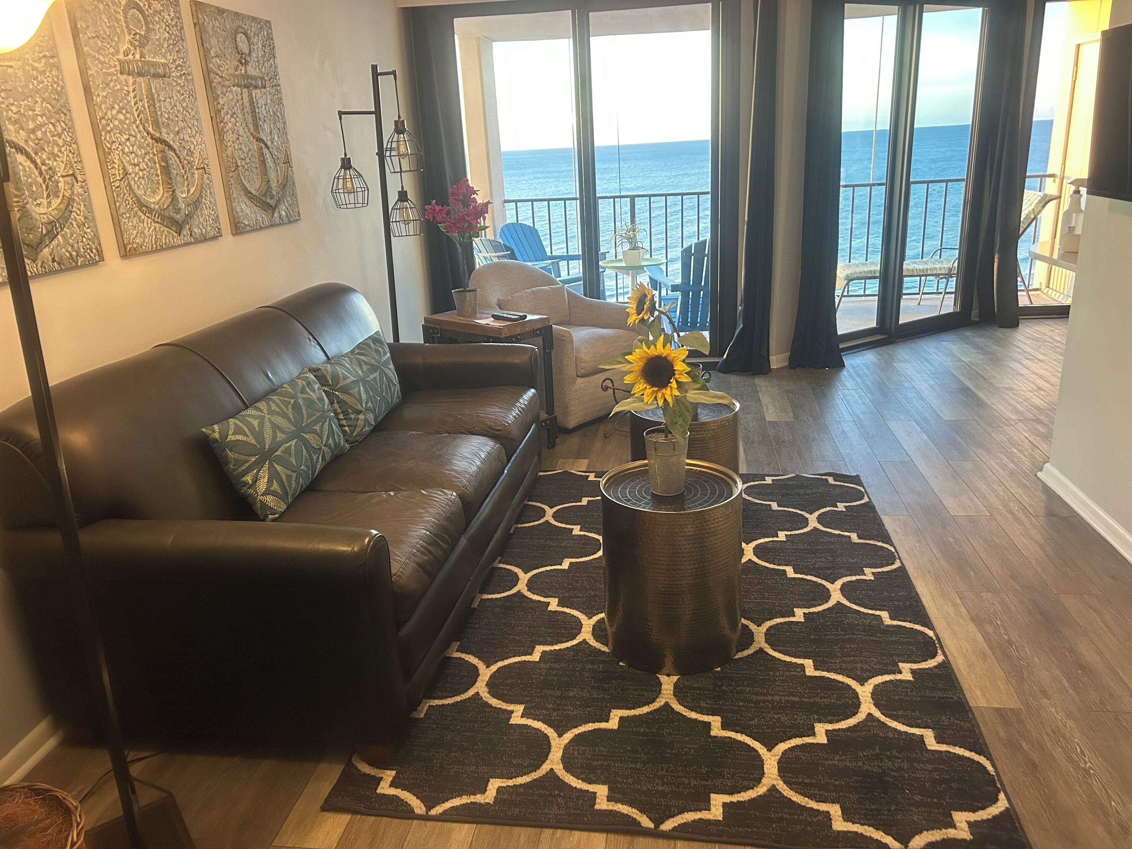 A living room with a leather sofa, a coffee table with a sunflower, and a view of the ocean through large windows.