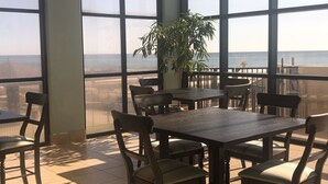 Un coin repas avec une grande table et des chaises, une plante en pot, et une vue sur la plage grâce à de grandes fenêtres.