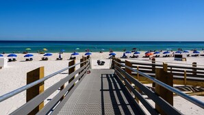 Une plage avec une promenade en bois menant au bord de l’eau, agrémentée de chaises longues et de parasols.