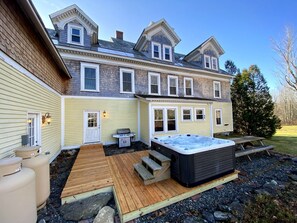Ein zweistöckiges Haus mit einer Terrasse, die ein Whirlpool, ein Grill und eine Holzterrasse umfasst.