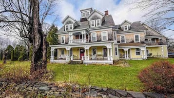 A large, two-story house with a front porch, multiple windows, and a stone wall in the foreground.