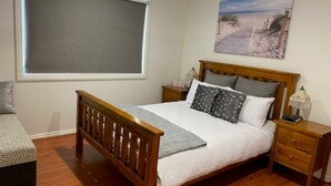Un dormitorio con una cama de madera, una mesita de noche con una lámpara, una silla y un cuadro con una playa.