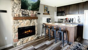 A kitchen with a stone fireplace, a bar area, and a flat-screen TV mounted above it. - ML 104 | Convenient Deck Access for Summer Escapes (Snowshoe)