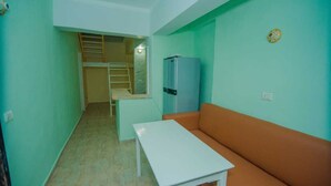 A small, compact room with a white table, an orange sofa, a blue refrigerator, and a wooden ladder leading to a lofted sleeping area. - Best location (Dahab)