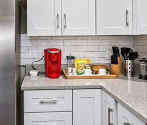 A kitchen with white cabinets, a red coffee maker, a wooden tray with tea bags, and a knife block.