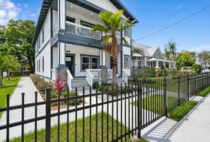 A two-story residential house with a front porch, a black metal fence, and a well-maintained lawn.