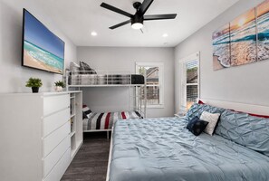 A bedroom with a bunk bed, a single bed, a ceiling fan, and artwork on the walls.