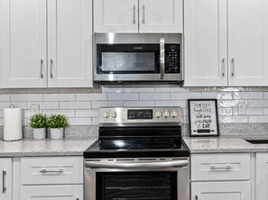 A kitchen with white cabinets, a stainless steel microwave, a stove, and a framed sign on the countertop. - Ybor City Group Home, Sleeps 12 | Emperor Castle: Game Room & Parking (Tampa)