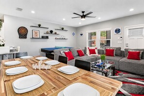 A modern living room with a ping pong table, grey sofas with red cushions, and a dining area with a wooden table set for six. - Ybor City Group Home, Sleeps 12 | Emperor Castle: Game Room & Parking (Tampa)