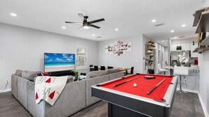 A modern living room with a pool table, grey sofa, and a flat-screen TV. - Ybor City Group Home, Sleeps 12 | Emperor Castle: Game Room & Parking (Tampa)