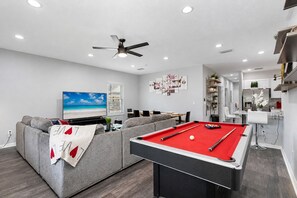 A modern living room with a pool table, grey sofa, and a flat-screen TV.