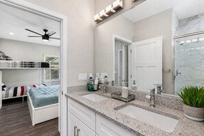 A modern bathroom with a large mirror, two sinks, a shower, and a ceiling fan.
