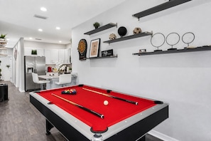 A modern kitchen with a built-in pool table, a dining area, and a living space with decorative shelves.