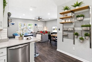 A modern kitchen with a built-in dishwasher, a dining area with a table and chairs, and a living room with a sofa and a ceiling fan. - Ybor City Group Home, Sleeps 12 | Emperor Castle: Game Room & Parking (Tampa)