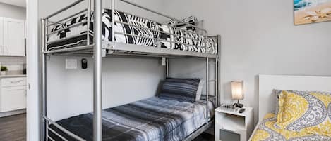 A bunk bed with a desk and chair, a bedside lamp, and a bed with patterned bedding.