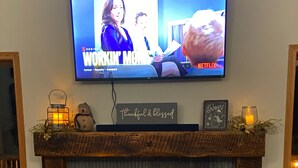 Una sala de estar con chimenea, televisor montado encima y adornos en la repisa.