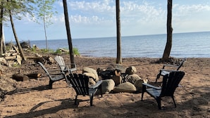 Un paisaje playero con dos sillas Adirondack, un hogar para fuego y vista al océano.
