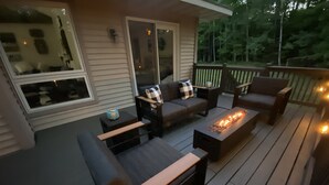Una terraza con mobiliario de madera oscura, que incluye un sofá, sillas y una mesa de centro. Hay un elemento decorativo tipo hogar en el centro.