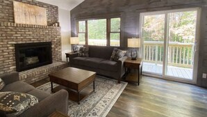 Una sala de estar con chimenea, un sofá, una mesa de centro y vistas a una terraza a través de amplios ventanales.