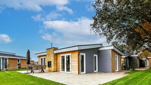 A modern house with a stone facade, a patio with outdoor furniture, and a well-maintained lawn. - Beautiful private villa for 6 guests with WIFI, A/C, pool, TV and terrace (Margraten)