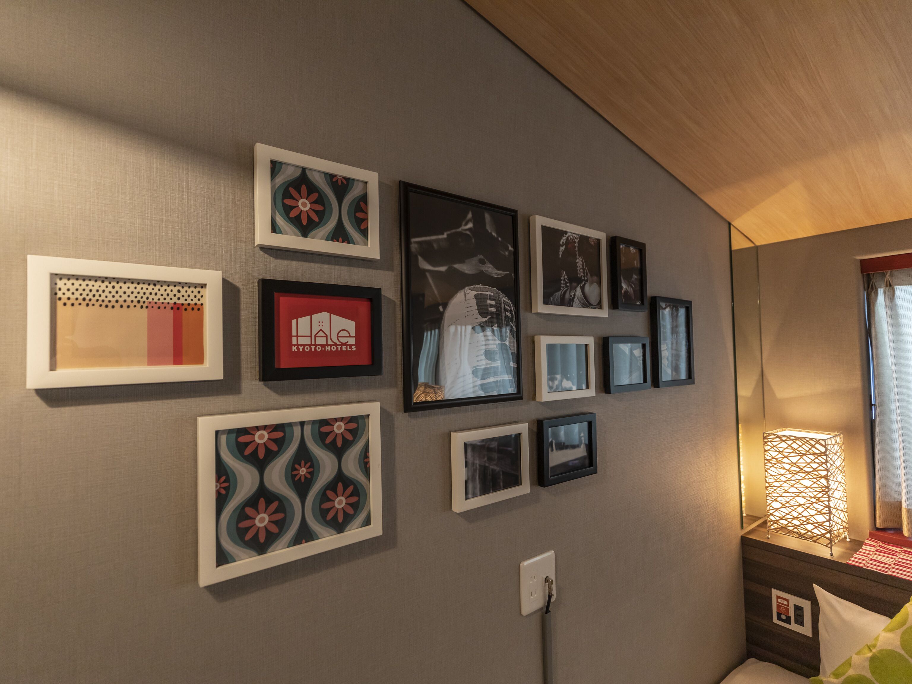 A hotel room with a wall decorated with various framed pictures and a bed with a green and white pillow.