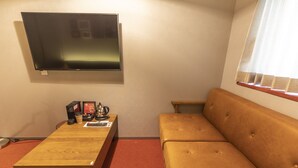 A room with a wooden coffee table, a sofa, a television mounted on the wall, and a window with blinds. - HALE Kyoto Toji (Kyoto)