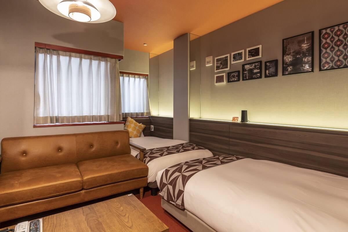 A hotel room with a sofa, two beds, a coffee table, and a wall with framed pictures.
