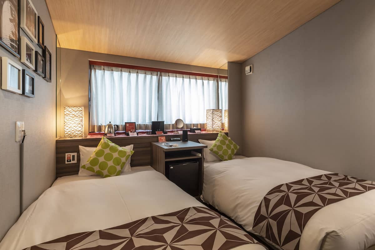A hotel room with two beds, a desk, and a window with curtains.