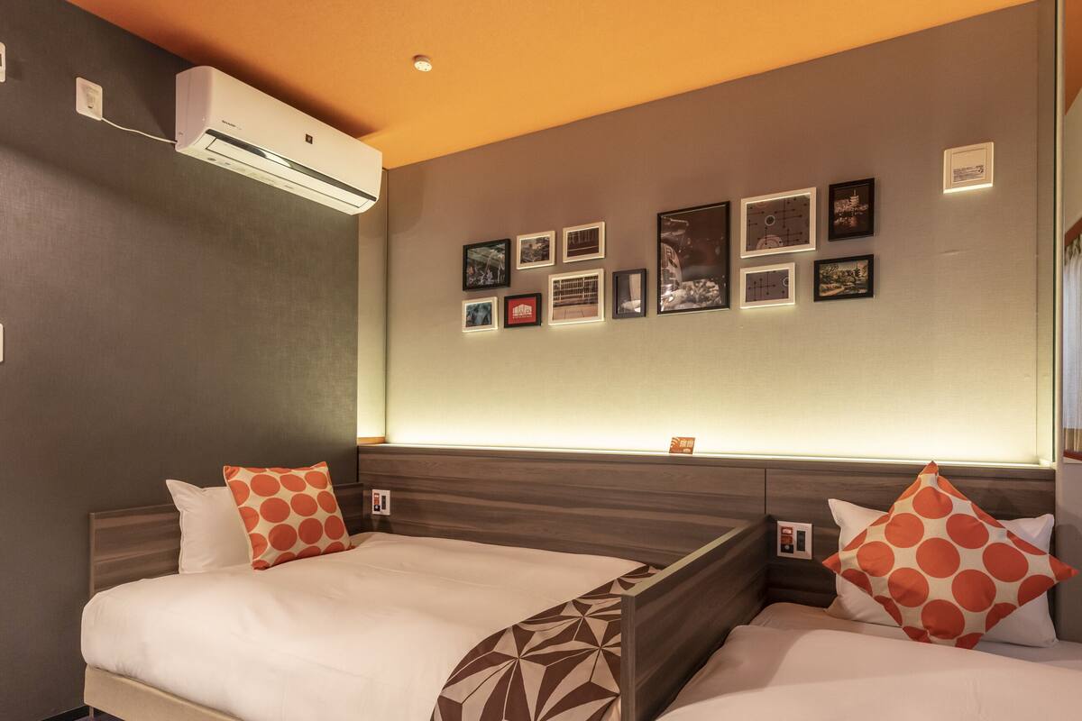 A hotel room with two beds, a wall-mounted air conditioner, and a series of framed pictures.